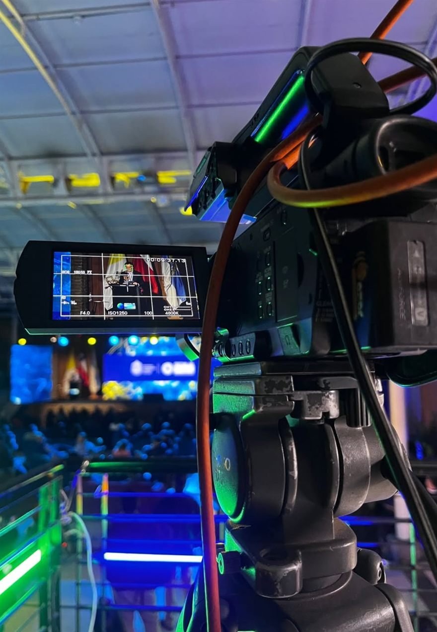 Detalle de cámara profesional con monitor abierto y cableado, registrando un evento iluminado.