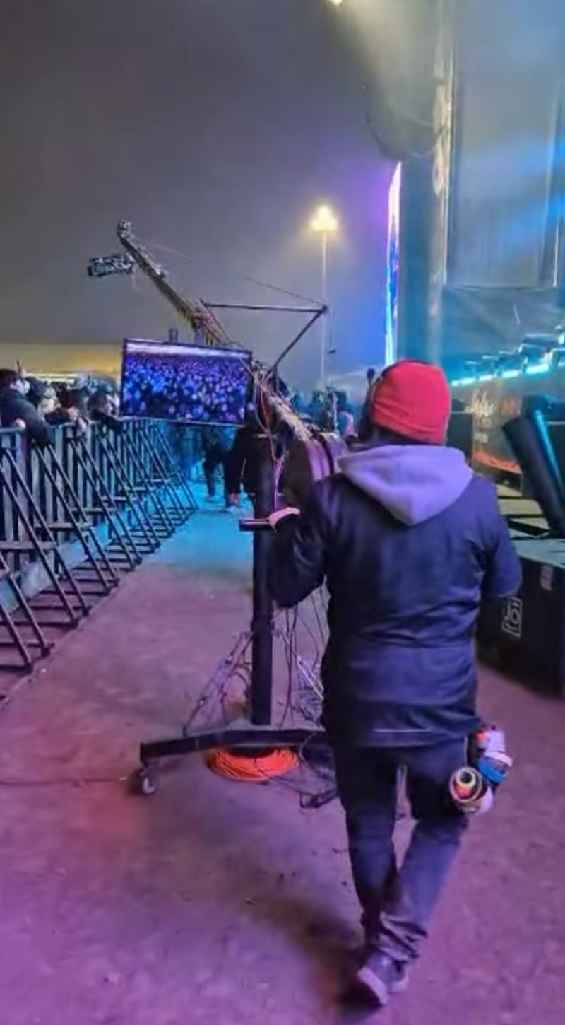 Técnico trasladando una pluma de cámara en el montaje de un evento al aire libre.