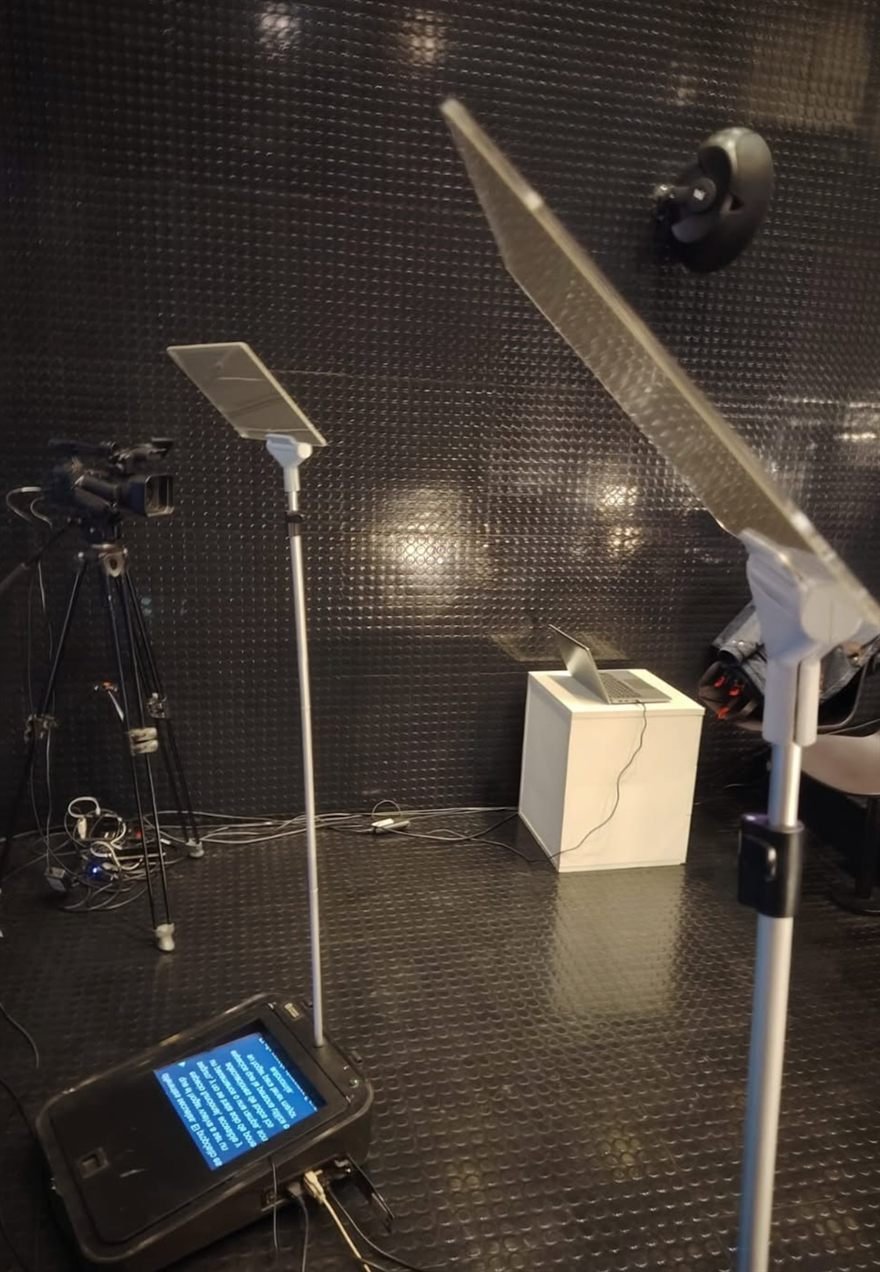 Teleprompter montado sobre trípode frente a un pódium, con cámara y monitor de apoyo.